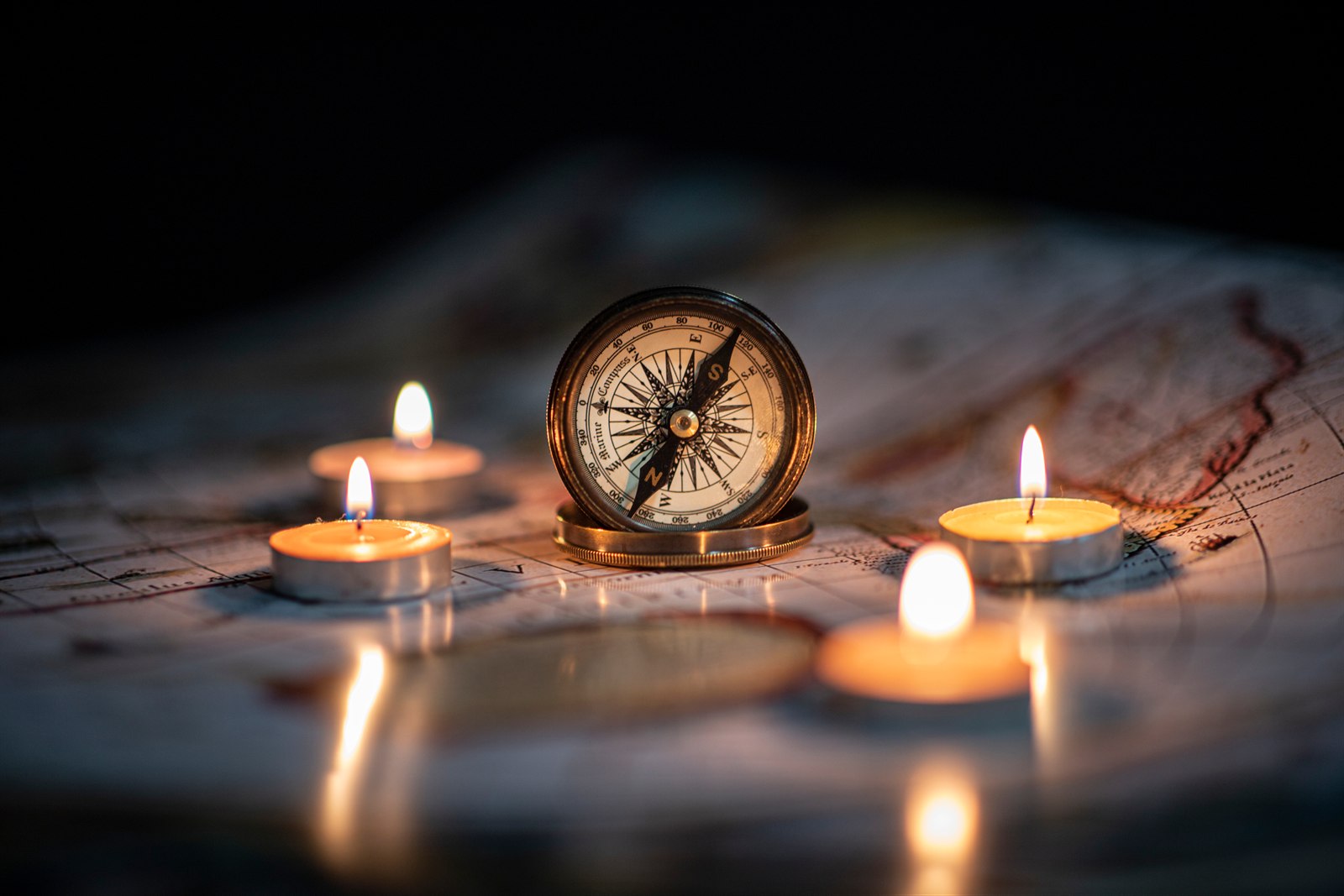 A brass compass on an old map between glowing candles