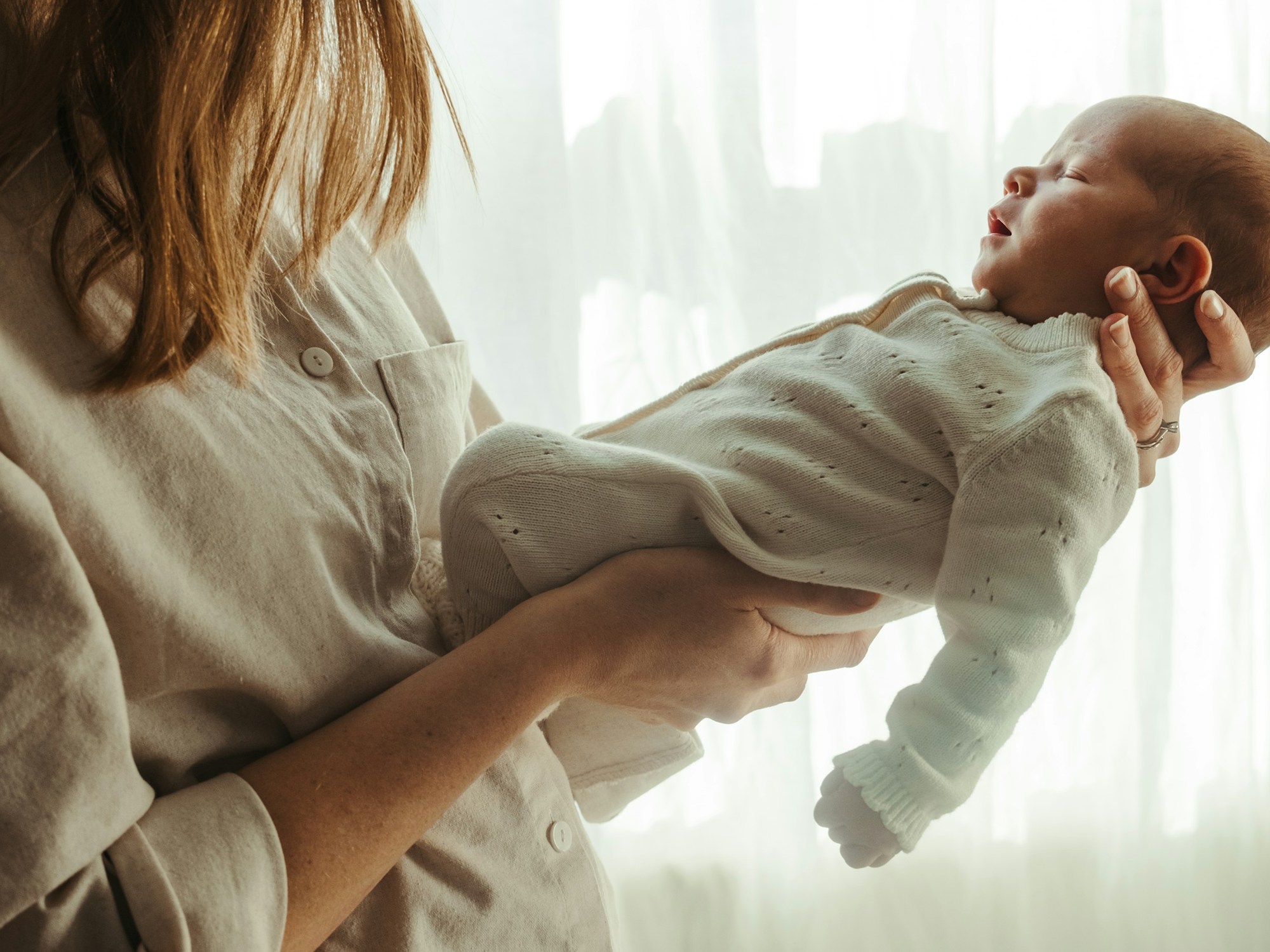 A mother holding her newborn baby by a sunny window