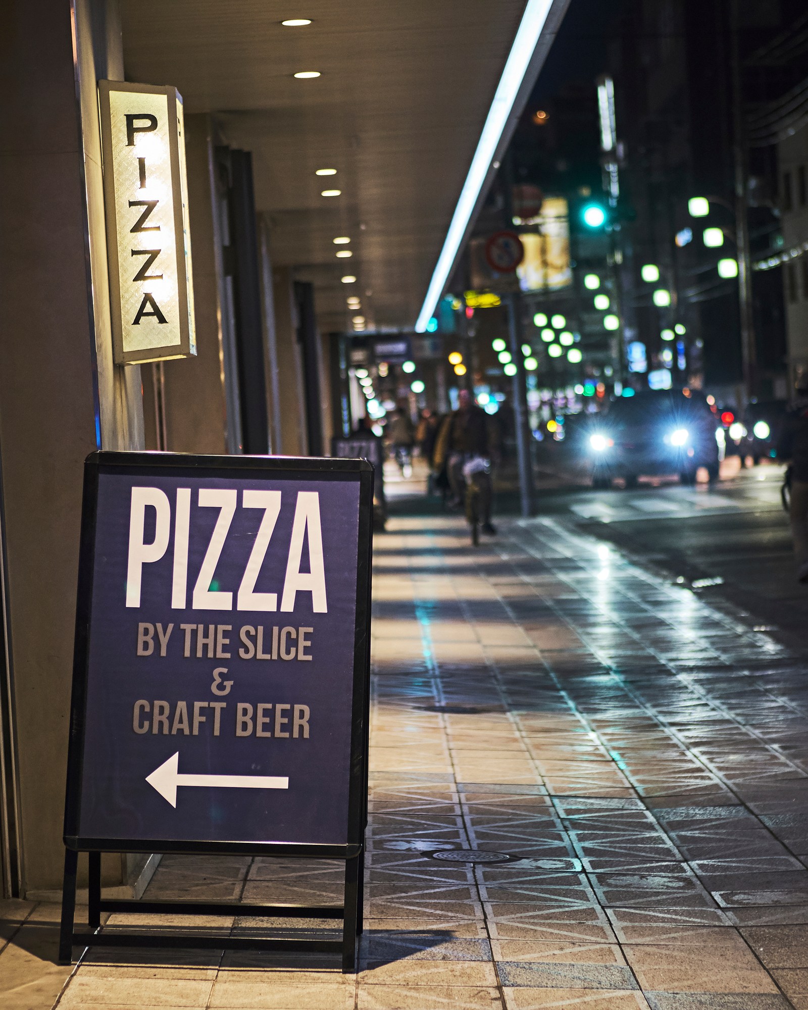 A lit-up pizza shop sign on a city sidewalk at night, the kind of local business people search for